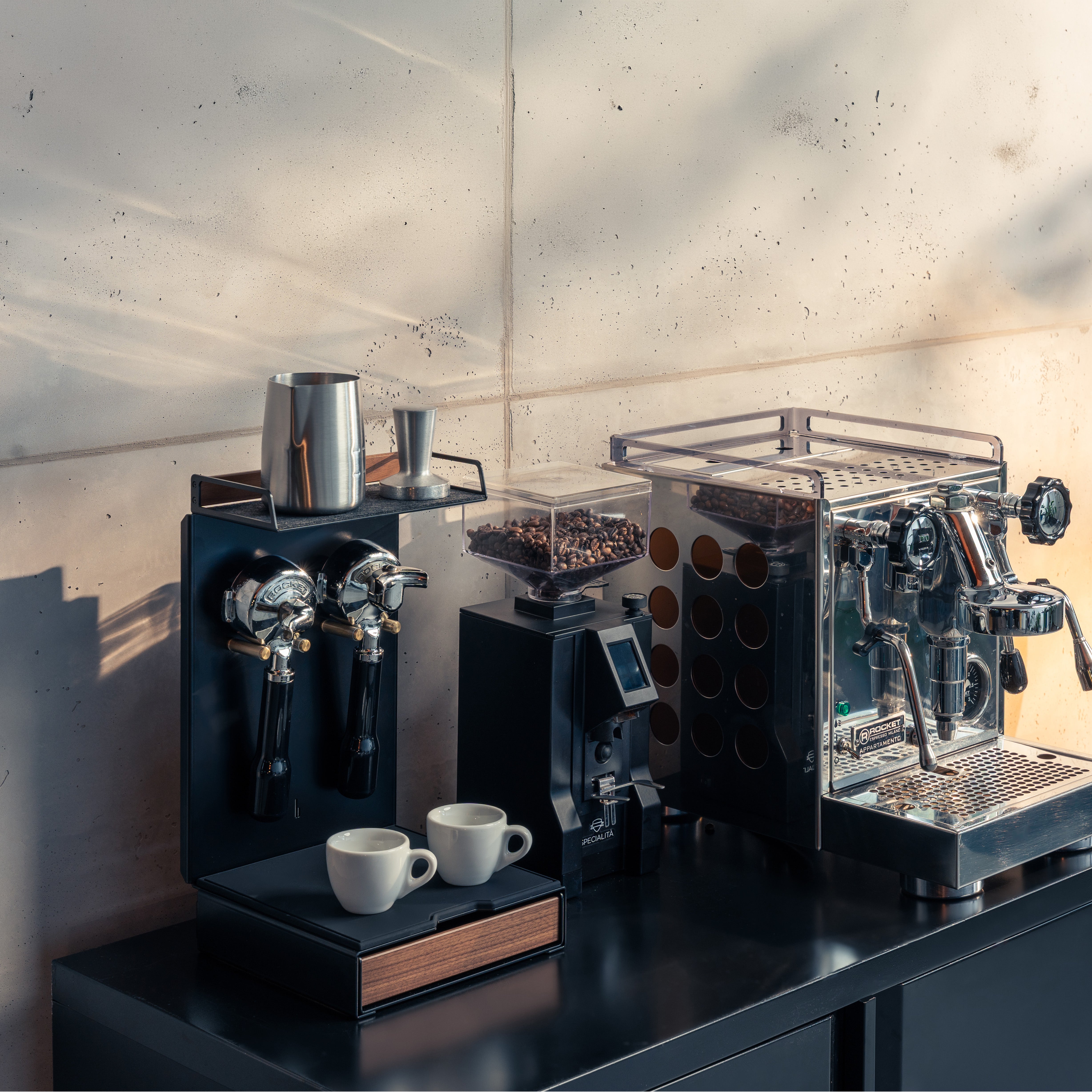 Barista Bar Nussbaum neben Espressomaschine und Kaffeemühle auf dunkler Küchenzeile, zwei Portafilter hängen an der Halterung, zwei Espressotassen auf der ausgezogenen Schublade