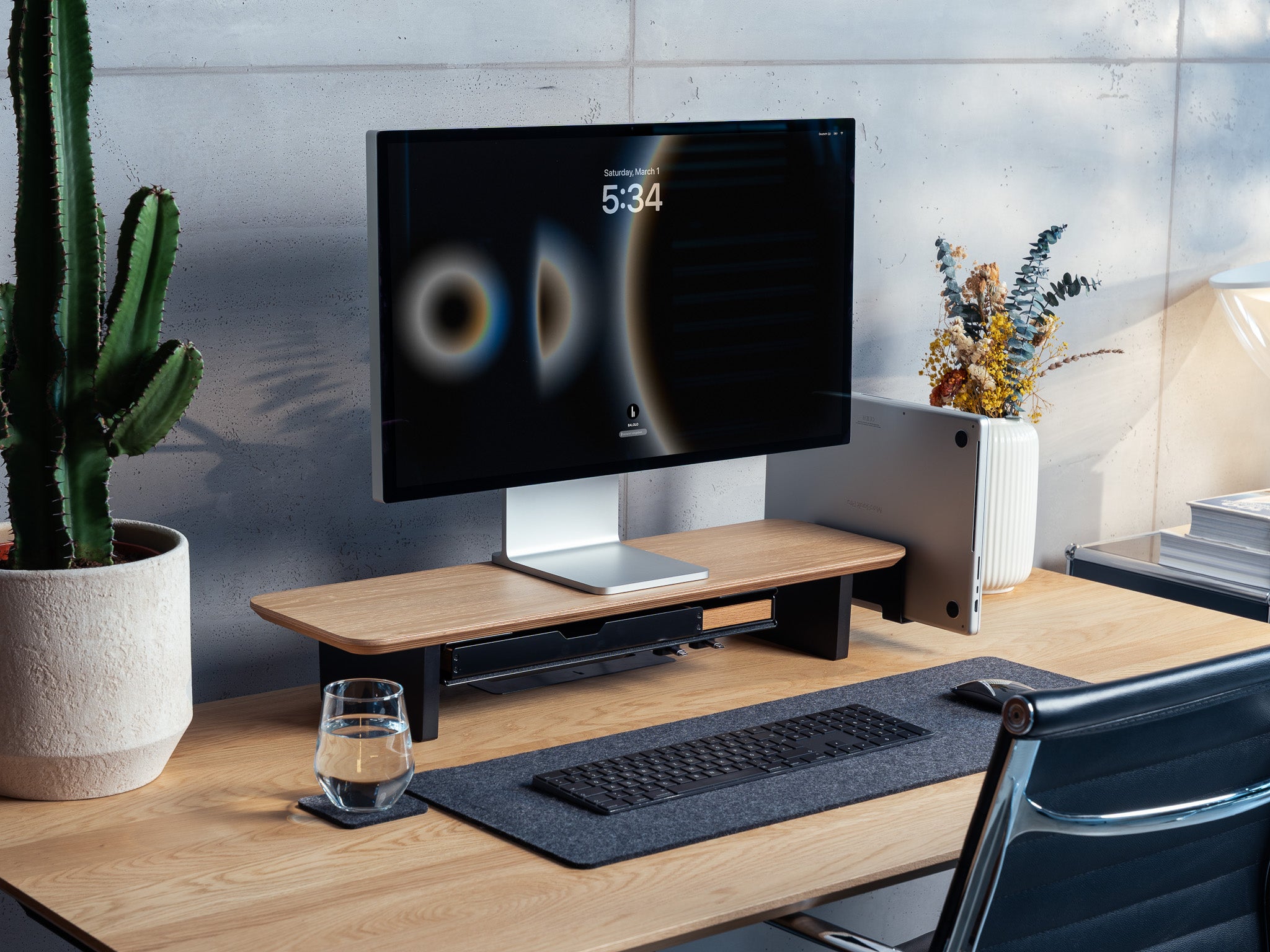 Setup Cockpit Monitorständer Medium aus Eiche mit Anbauteilen: Laptop Dock, großes Fach mit Stiftablage Large und Stiftablage, Kabelmagneten, Desk Pad Large und Desk Coaster. Abgebildet mit Apple Studio Display, Macbook, Tastatur und Maus. Abgebildet auf einem Schreibtisch aus Eiche in einem modernem, hellen Office Setting. @expand