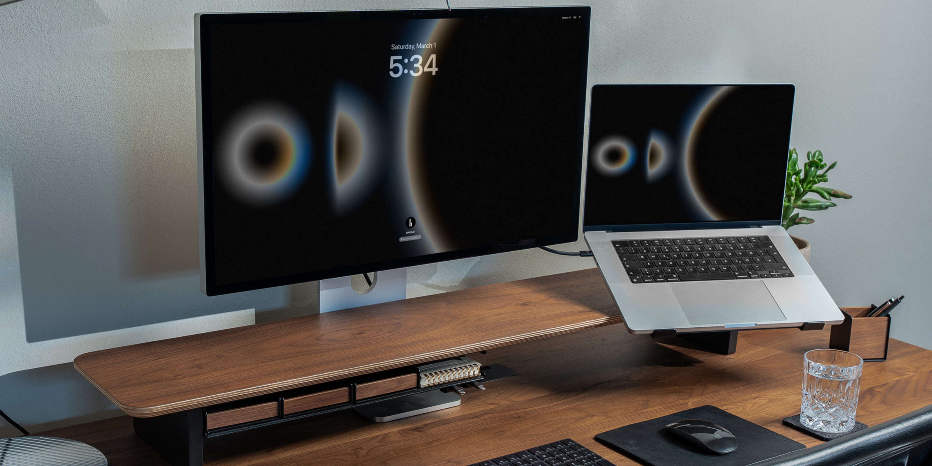 Setup Cockpit Monitorständer in Nussbaum auf einem Nussbaum Schreibtisch mit integriertem Laptophalter und Fach im modernen Office Setting.