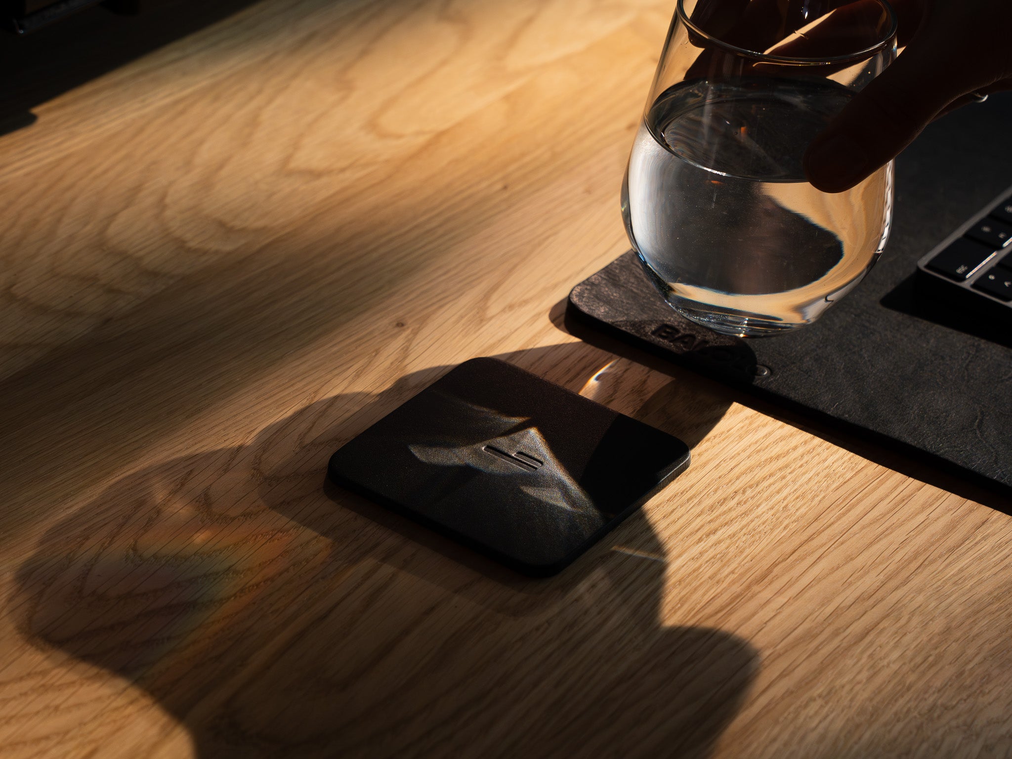 Detailaufnahme des Leder Untersetzers. Inszeniert auf einem Eiche Schreibtisch, neben einem Leder Desk Pad. Person stellt ein Wasserglas auf den Untersetzer.