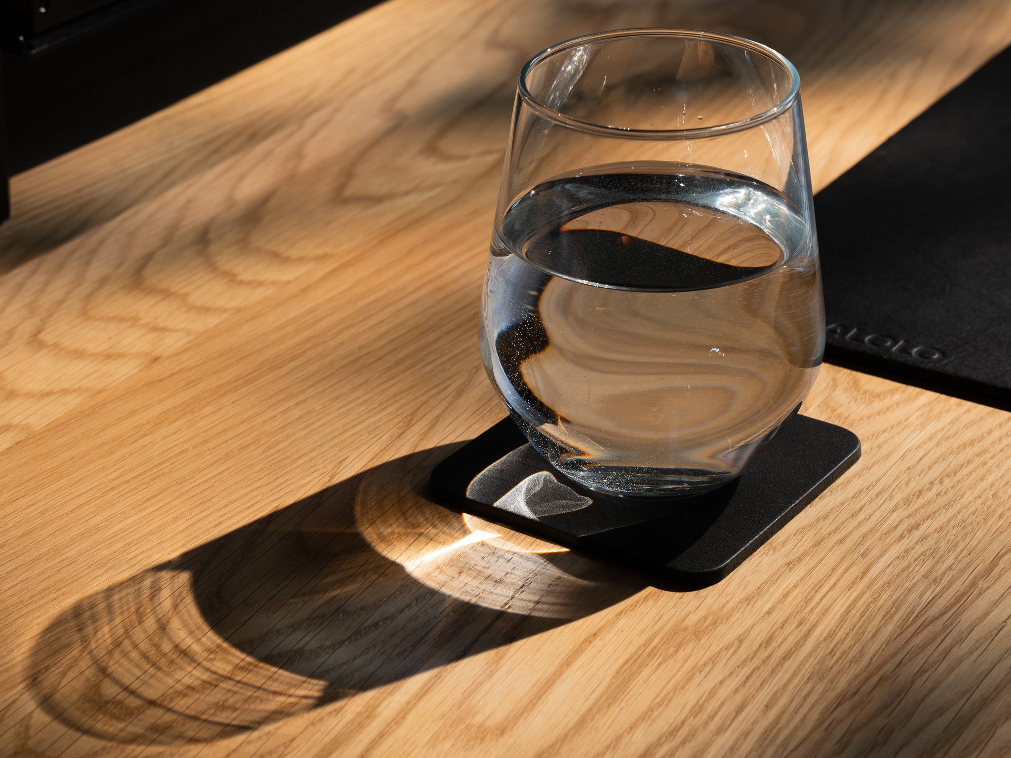 Detailaufnahme des Leder Untersetzers. Inszeniert auf einem Eiche Schreibtisch, neben einem Leder Desk Pad. Auf dem Untersetzer steht ein Wasserglas.