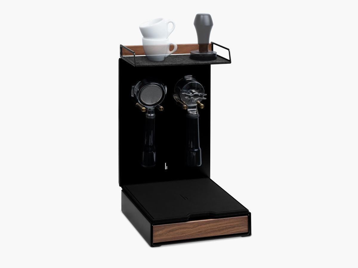 Barista Bar in Schwarz mit Nussbaum-Holzablage, zwei Espressotassen und Tamper auf der Filzauflage, zwei leere Portafilter-Halterungen darunter, Schublade mit Nussbaum-Front @expand #material_Amerikanischer Nussbaum
