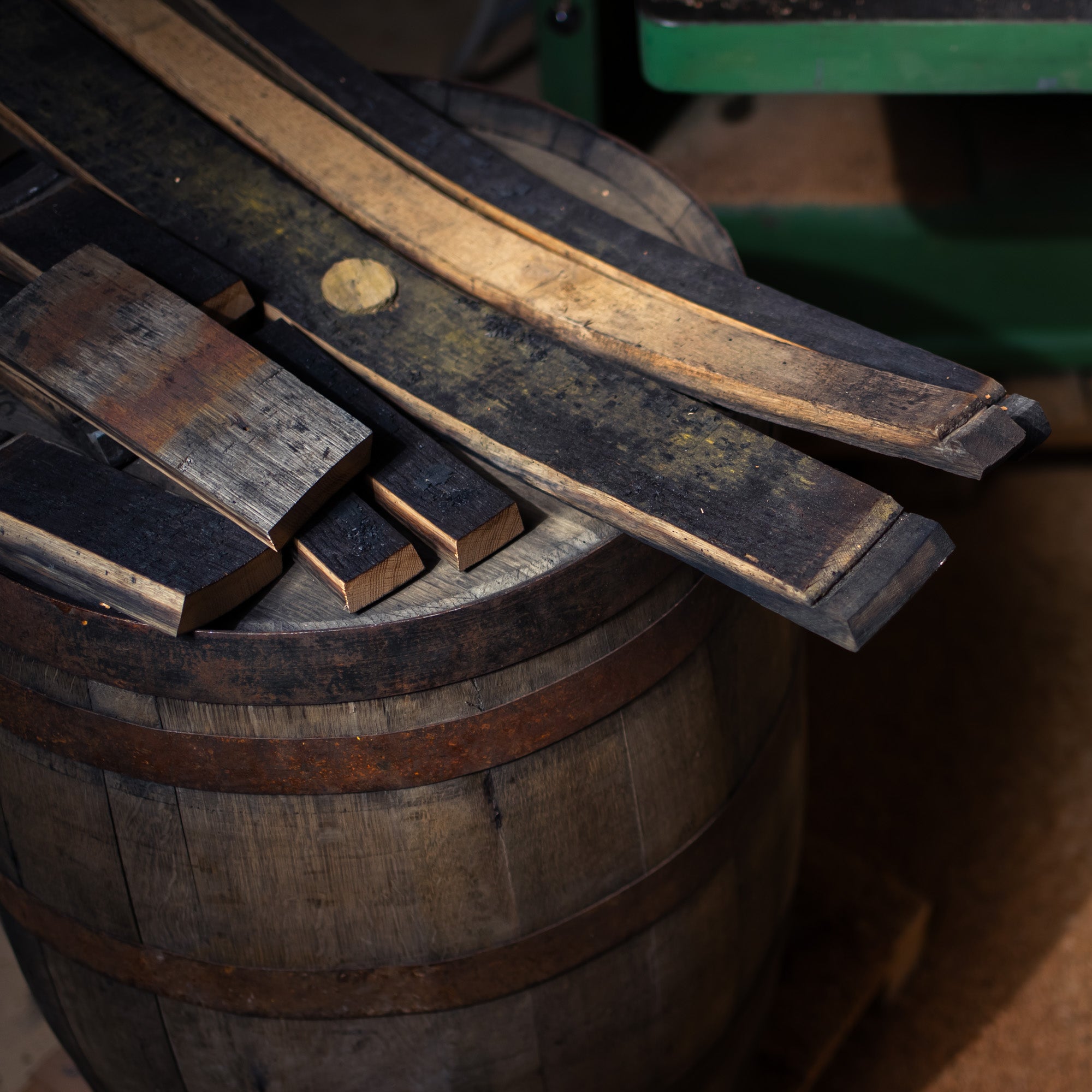 Detailaufnahme von Fassdauben, die auf einem Whiskeyfass liegen. In atmosphärischer Werkstatt inszeniert. 