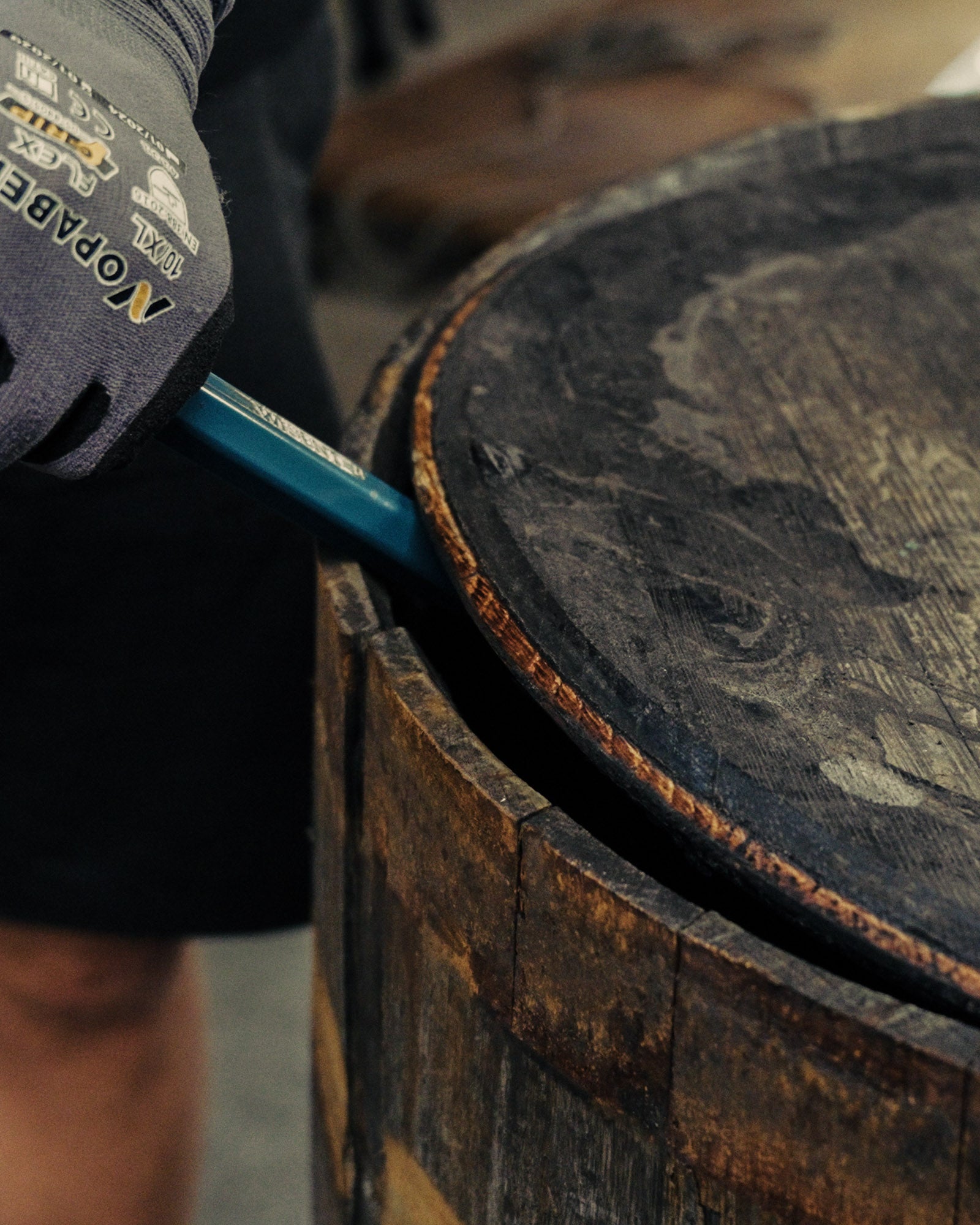 Stimmungsvolle Detailaufnahme eines Whiskeyfass, Deckel wird geöffnet mit Eisenstange. 